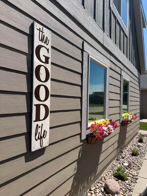 Un edificio con un letrero que dice 'the GOOD life' y macetas con flores en las ventanas.