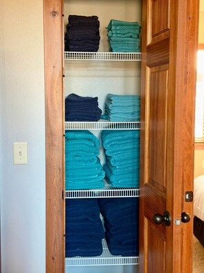 A closet with shelves holding folded towels in various shades of blue and black. - The Good Life - Okoboji cabin in Bridges Bay (Arnolds Park)