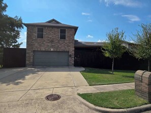 A two-story house with a garage, a front yard with a lawn, and a tree. - Movie Room | Huge Patio|Hot Tub|Near Lake & Frisco (Little Elm)