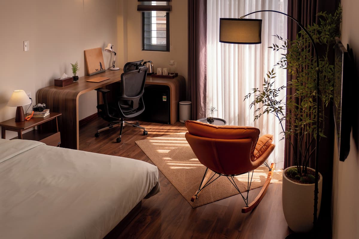 Een hotelkamer met een bed, bureau, stoel, lamp en een plant in pot.