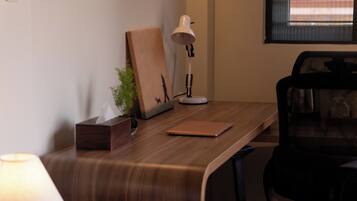 A wooden desk with a laptop, a white desk lamp, a framed picture, and a small plant.