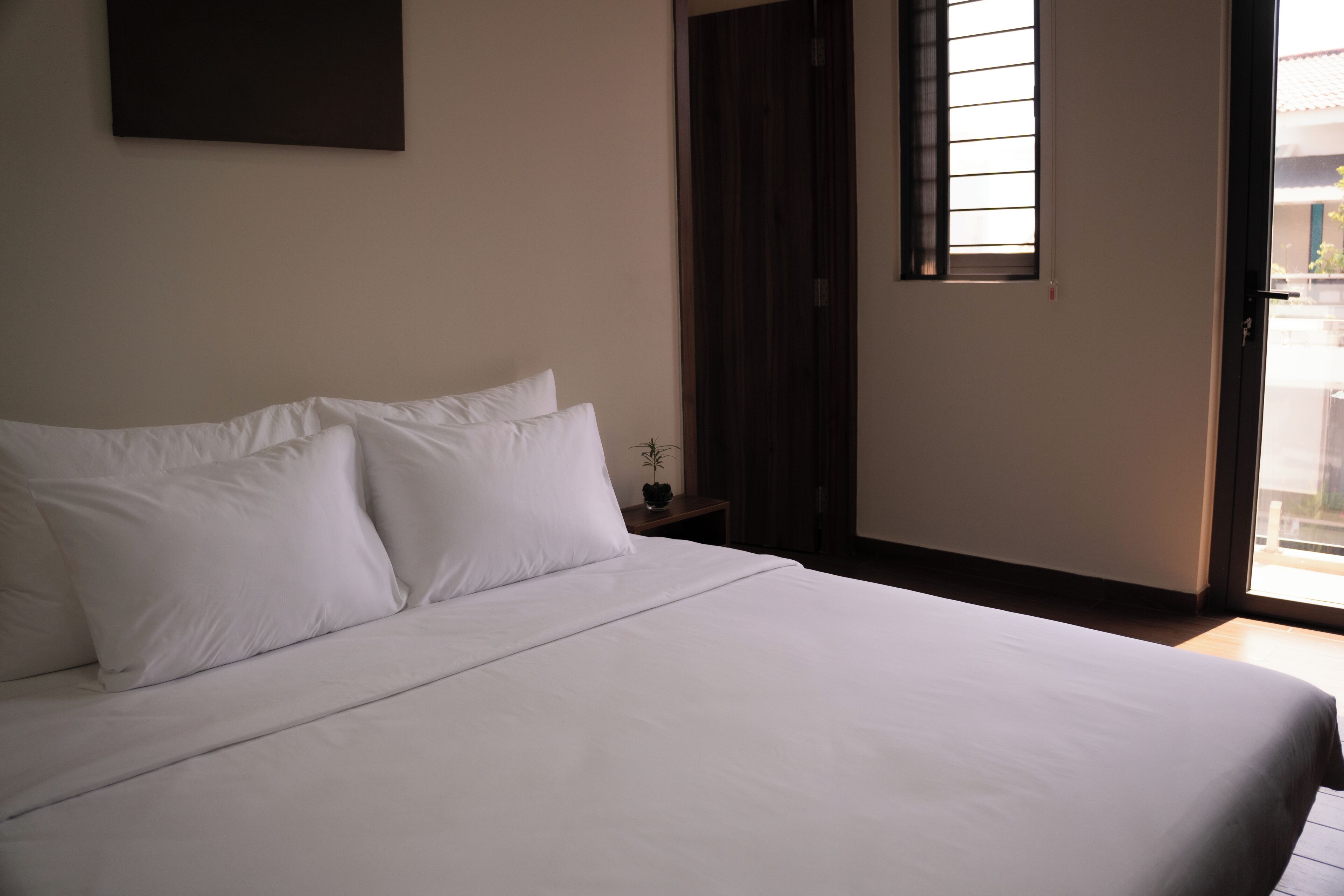 Una cama bien hecha con sábanas blancas en una habitación con suelo de madera y una mesita de noche pequeña.