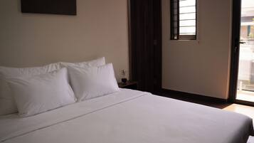 Una cama bien hecha con sábanas blancas en una habitación con suelo de madera y una mesita de noche pequeña.