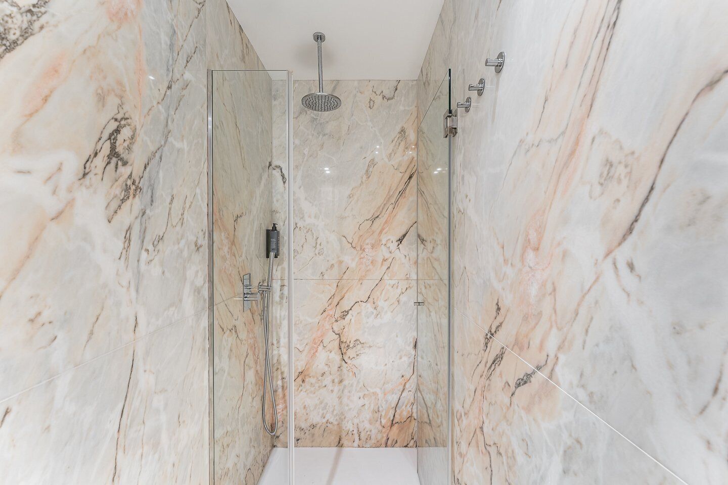 A modern bathroom with a glass-enclosed shower, marble walls, and a white bathtub.