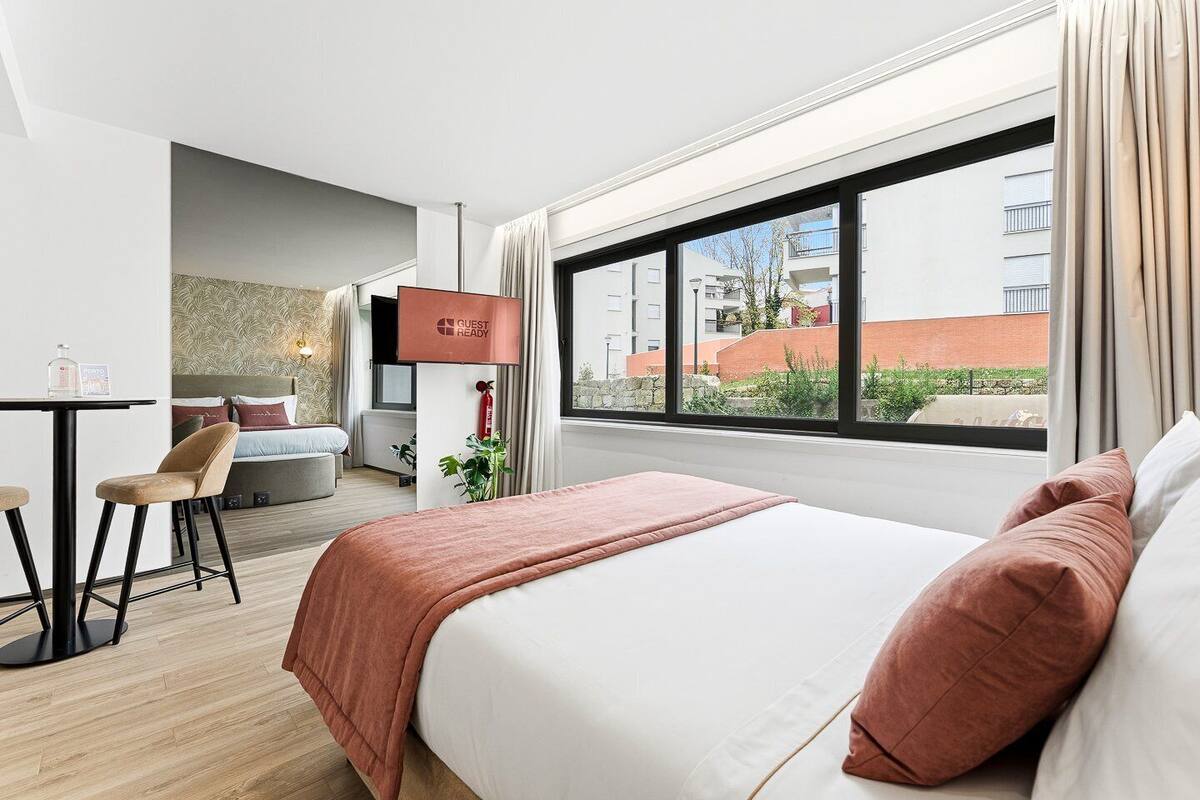 Habitación de hotel con cama, escritorio, silla y ventana con vista a edificios.