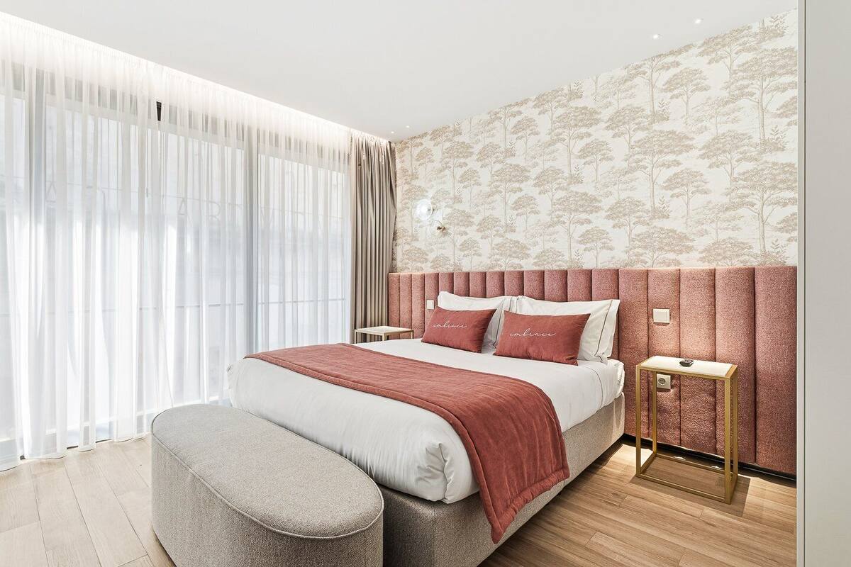Un dormitorio moderno con una cama grande, un banco, una mesita de noche y un papel tapiz estampado.