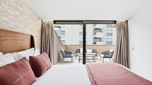 A modern hotel room with a large bed, a balcony with seating, and a view of the cityscape. - Guestready - Alma Invicta (Porto)