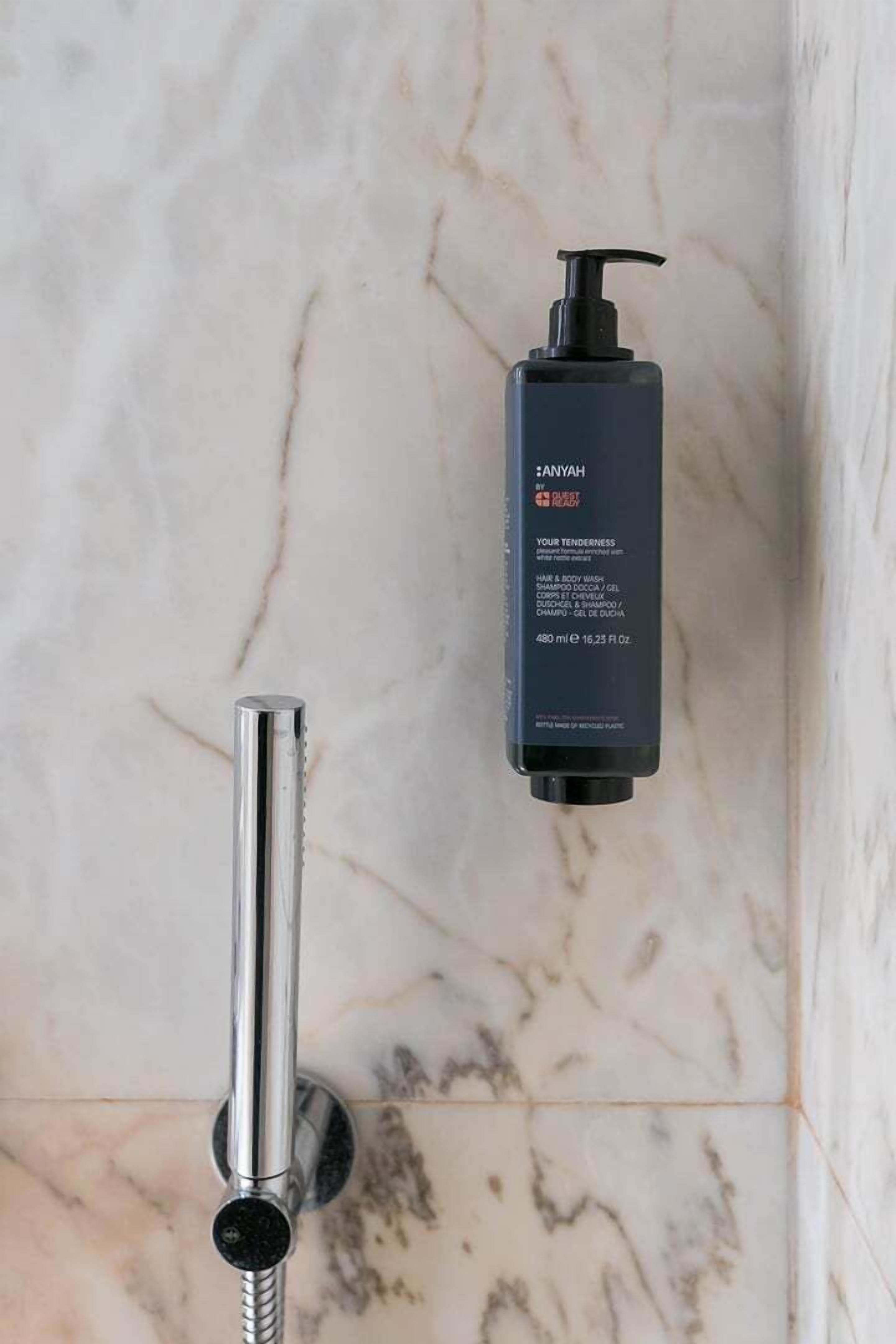 Un bagno con pavimento in marmo, soffione cromato e una bottiglia di shampoo nera.