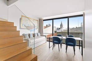 Un appartamento moderno con una scala, un divano, un tavolo da pranzo con sedie e ampie finestre che si affacciano sulla città.