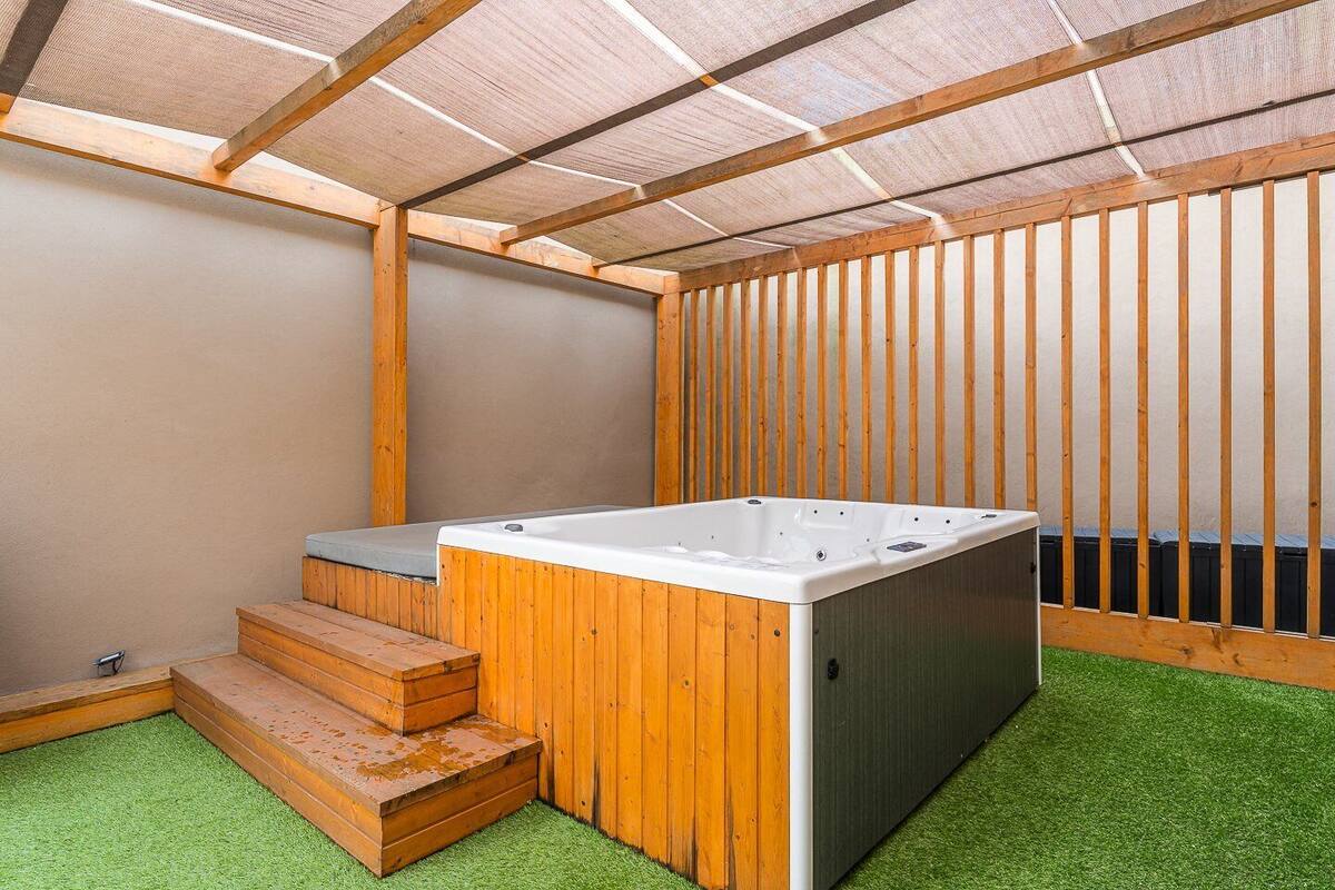 Un jacuzzi en un espacio exterior cubierto con escalones de madera y césped artificial.