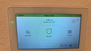 Honeywell Home -turvajärjestelmän ohjauspaneeli, jossa on vihreä virtailmaisin. Näytöllä näkyy aika 5.36, päivämäärä 1. heinäkuuta 2013 sekä kuvakkeet, jotka edustavat multimediaa, turvallisuutta ja laitteita.