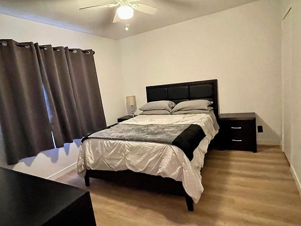 Une chambre à coucher comprenant un lit, des tables de chevet, un bureau et un ventilateur de plafond.