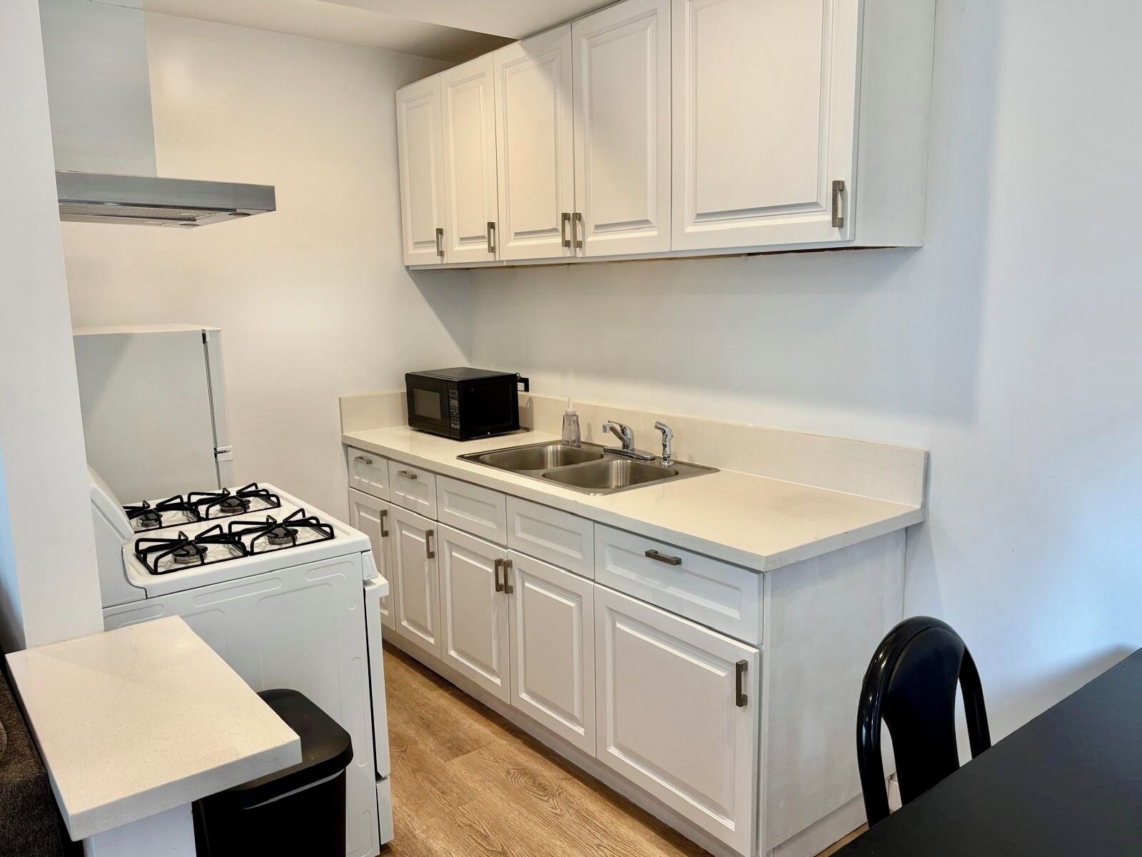 A compact kitchen with white cabinets, a gas stove, a microwave, and a sink.