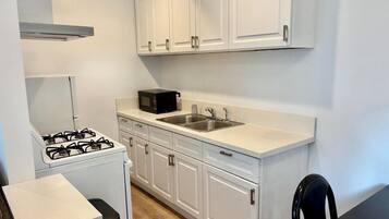 A compact kitchen with white cabinets, a gas stove, a microwave, and a sink.