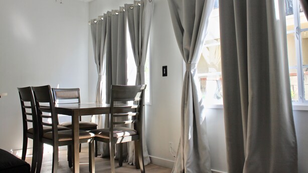 A dining area with a table and chairs, a ceiling fan, and curtains on the windows. - SMA Apartments (Santa Monica)