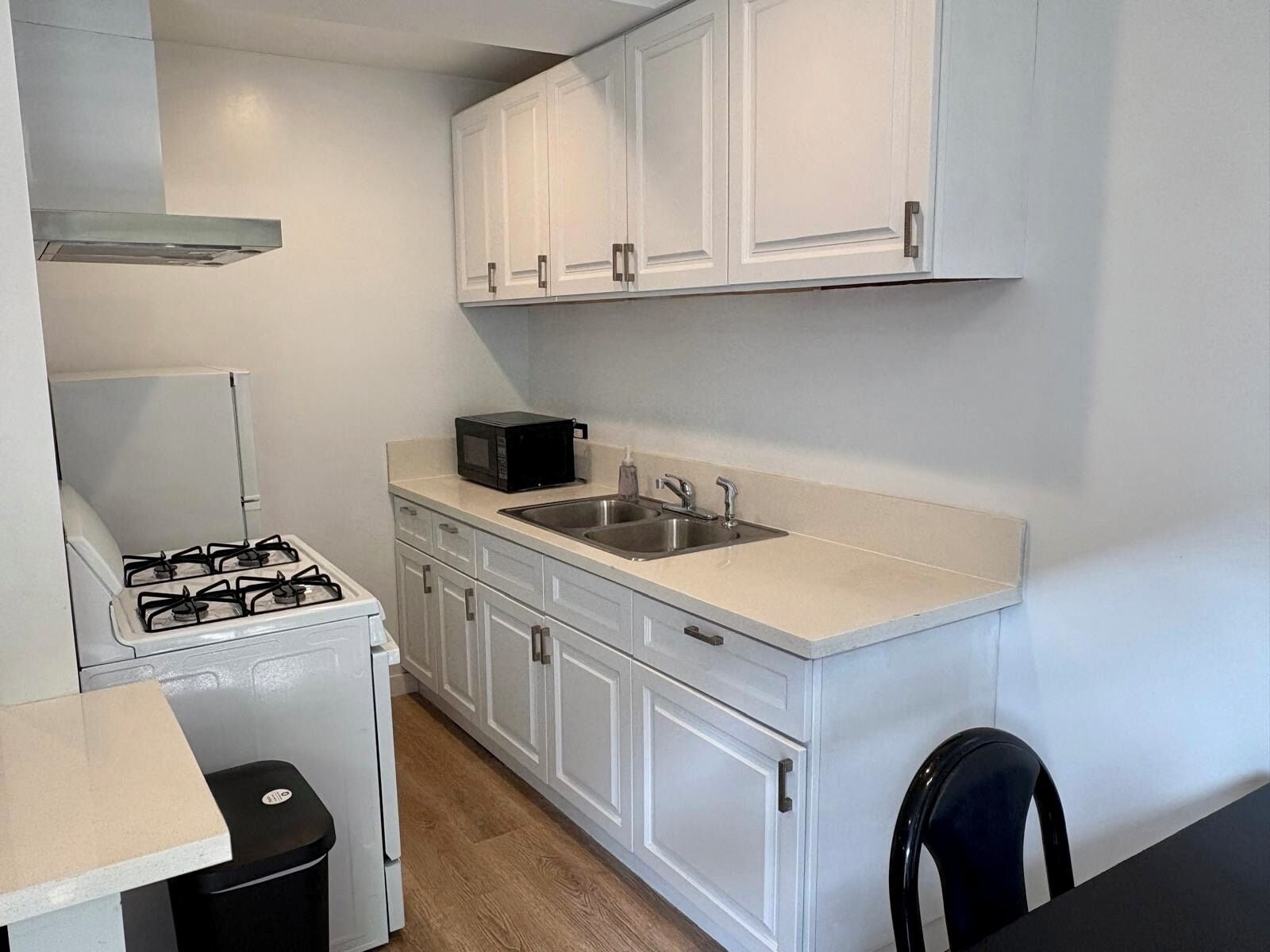 Cocina compacta con armarios blancos, estufa a gas, microondas y un lavabo.