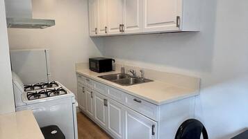 Cocina compacta con armarios blancos, estufa a gas, microondas y un lavabo.