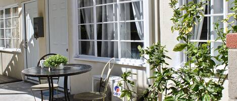 En terrasse med et bord, stole, en potteplante og et vindue med gardiner.