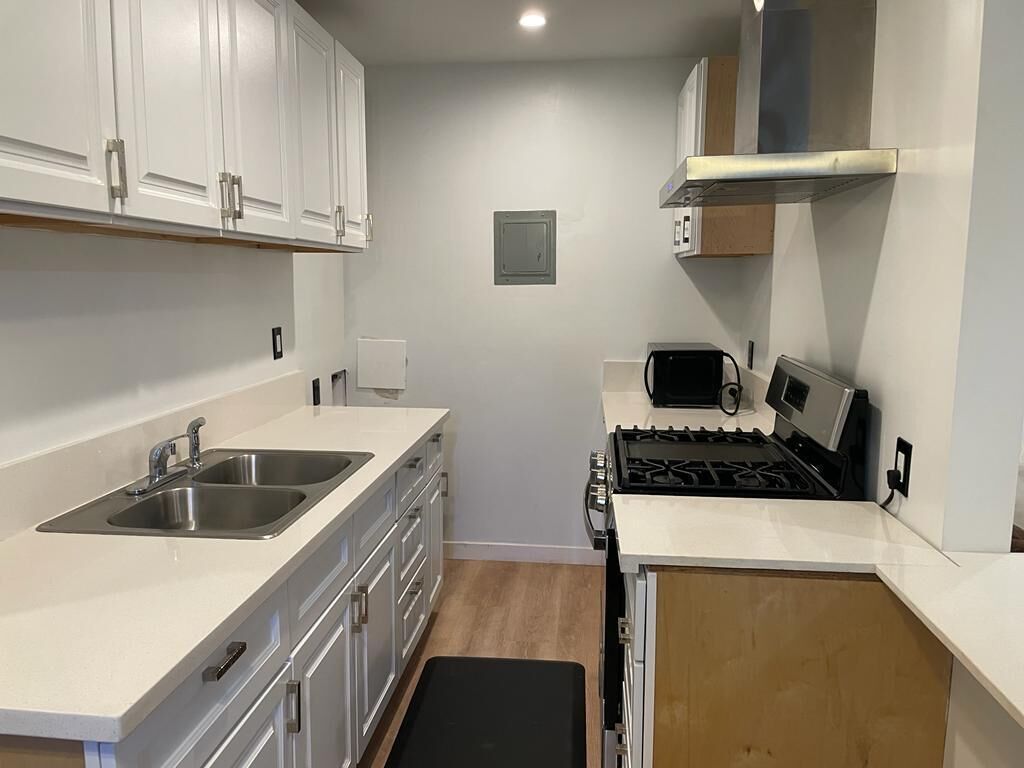 A compact kitchen with white cabinets, a double sink, a stove, and a microwave.