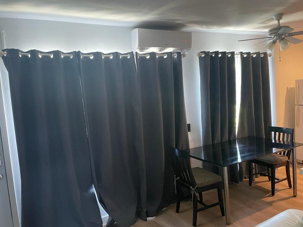 Een kamer met een glazen tafel en stoelen, een plafondventilator en zwarte gordijnen.