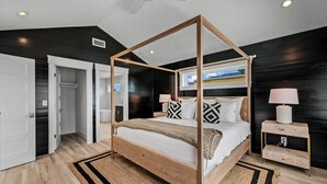 Una cama con dosel de madera, ropa de cama blanca y almohadas estampadas.