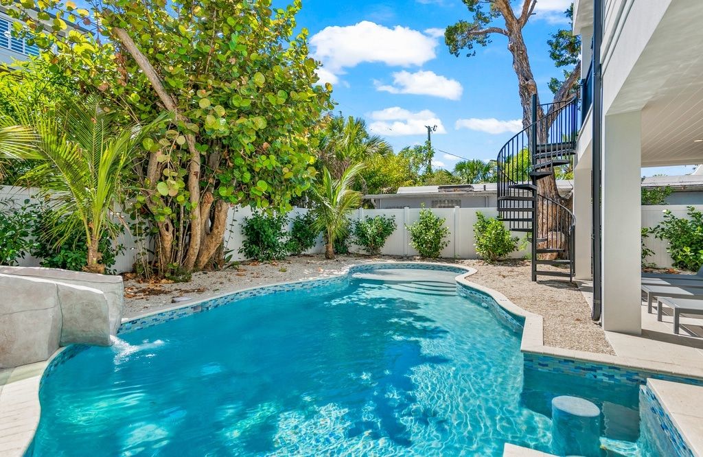 A swimming pool with a curved edge, surrounded by a variety of trees and shrubs.