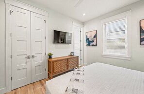 Ein Schlafzimmer mit einem Bett, einem Holzschrank, einem an der Wand befestigten Fernseher und einem Fenster mit Jalousien.