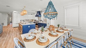 Cocina moderna con armarios blancos, una isla azul y un comedor con una mesa grande dispuesta para seis personas.
