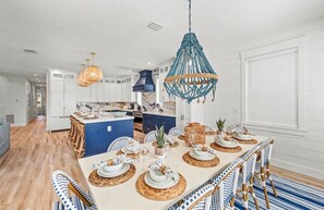 A modern kitchen with white cabinetry, a blue island, and a dining area with a large table set for six. - Stunning Home w/ Pool, Slide & Spa & Rooftop Views (Sarasota)