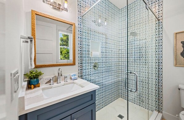Un bagno con cabina doccia in vetro, un lavandino bianco e uno specchio con cornice in legno.