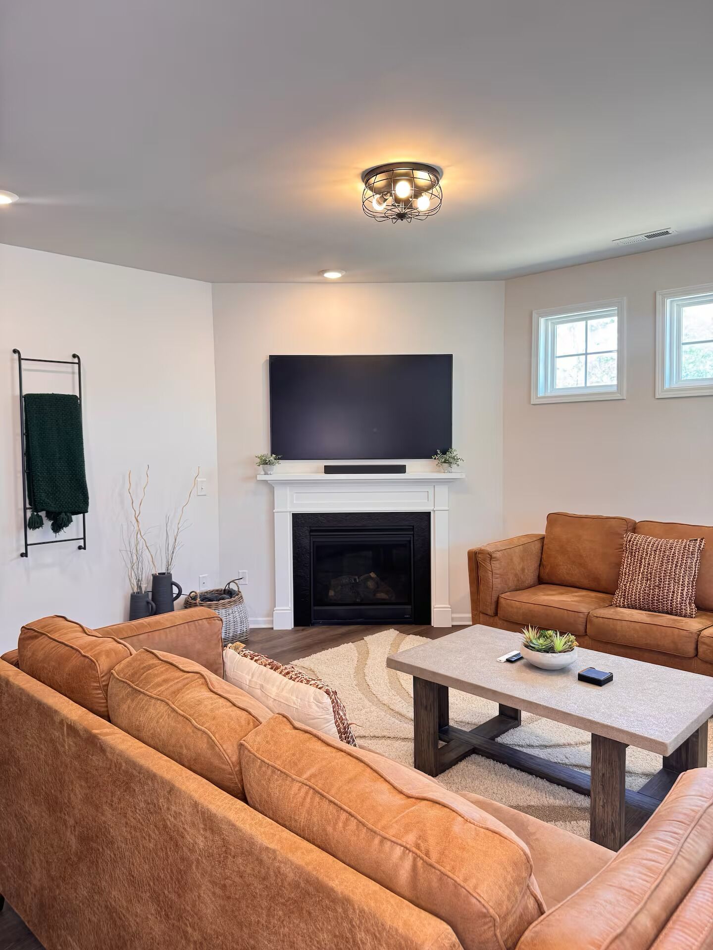 A living room with a fireplace, a large flat-screen TV, a brown leather sofa, and a coffee table.