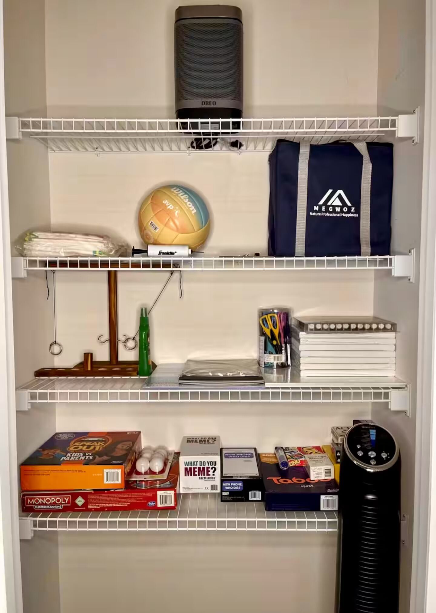 A shelf with a volleyball, a t-shirt, board games, and a speaker.
