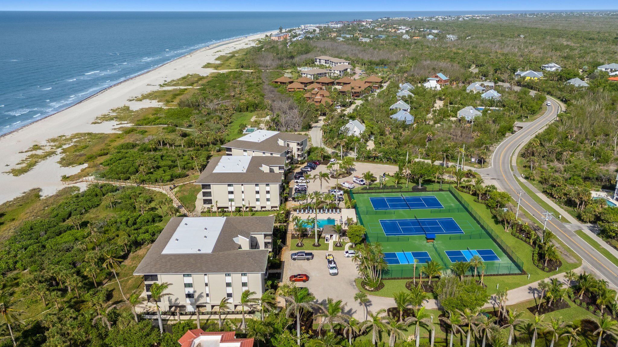 An aerial view of a coastal hotel with multiple buildings, a beach, and tennis courts.