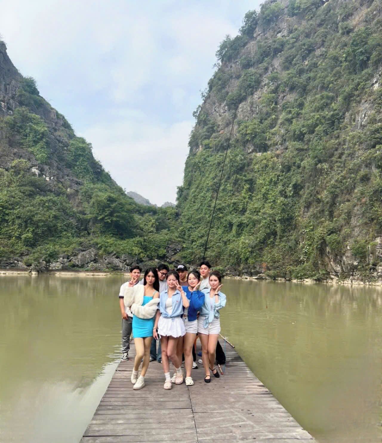A group of people standing on a wooden dock by a calm river, surrounded by lush green hills.