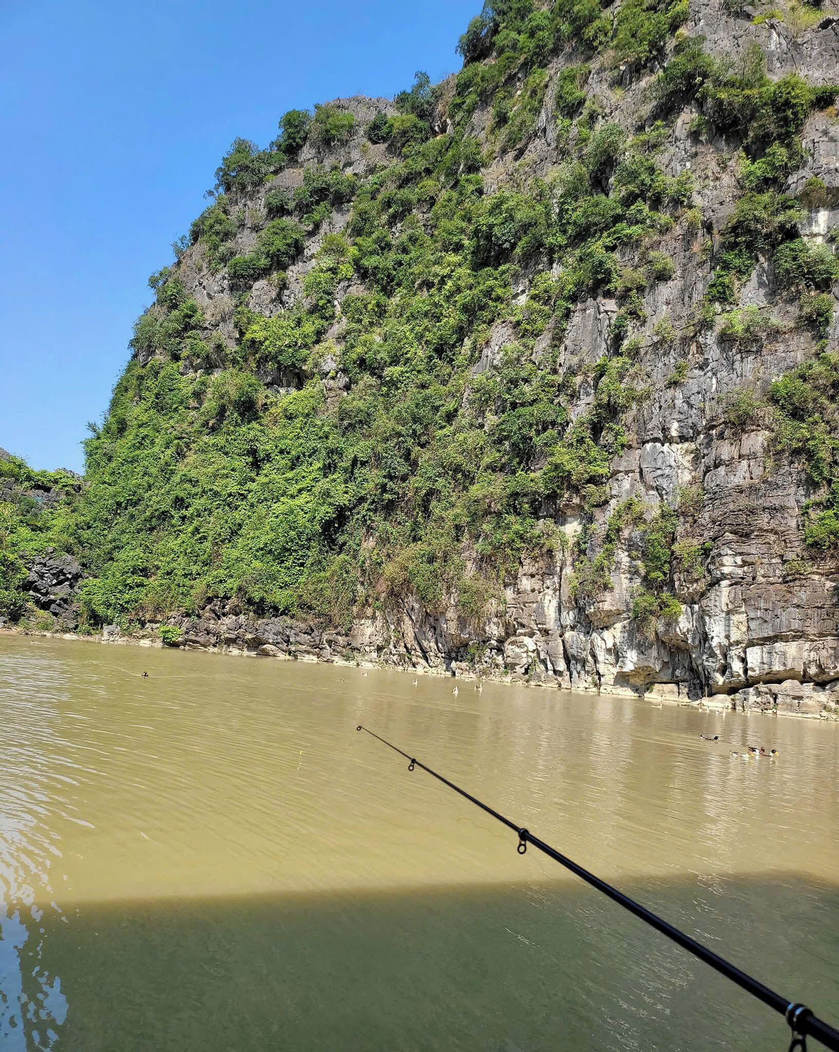 Una canna da pesca in un fiume tranquillo, con una scogliera rocciosa sullo sfondo.