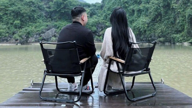 Two people sitting on a wooden dock with chairs, overlooking a river with steep, green hills in the background. - Thien Truong An Eco Green Valley (Tay Hoa Lu)