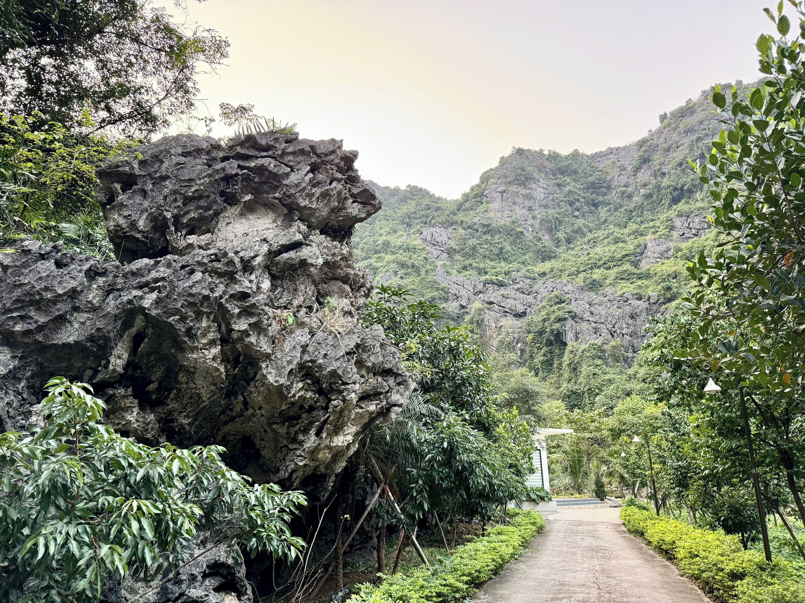 A pathway leading through a lush, green landscape with a large rock formation on the left.
