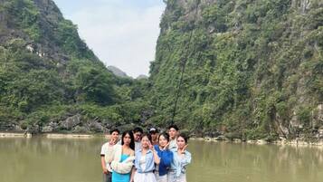A group of people standing on a wooden pier extending into a calm river, surrounded by lush green hills.