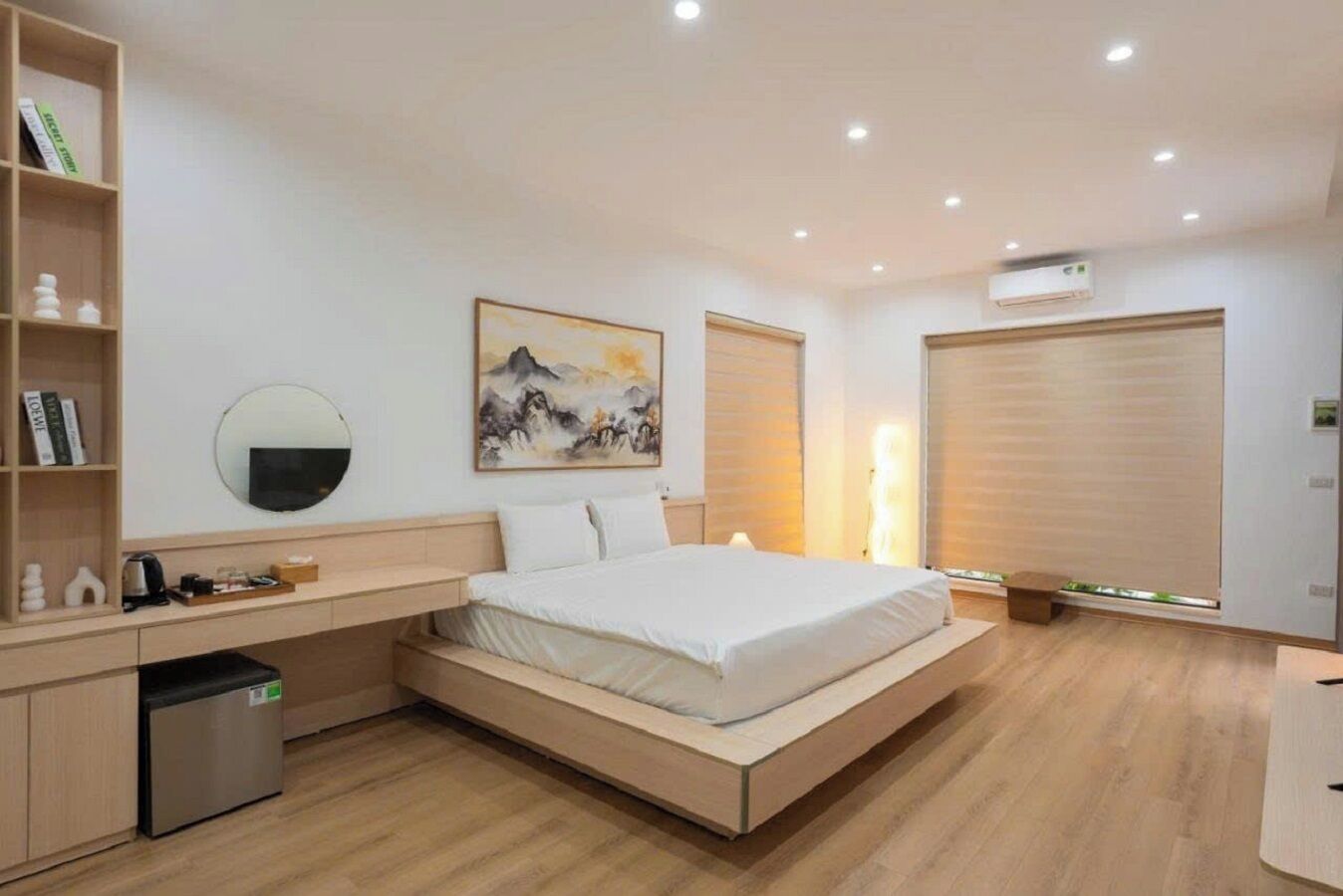 A modern bedroom with a bed, bedside table, bookshelf, and artwork.