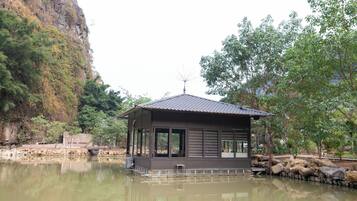 A floating house with a tiled roof, large windows, and a small antenna on top, surrounded by water and greenery.