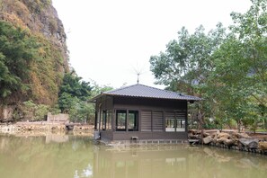 Een drijvend huis met een pannendak, grote ramen en een kleine antenne bovenop, omgeven door water en begroeiing.