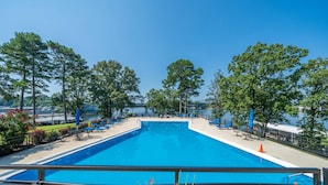 Una piscina rectangular con superficie de agua azul cristalina, rodeada por una terraza con sillas de descanso y vistas a un cuerpo de agua.