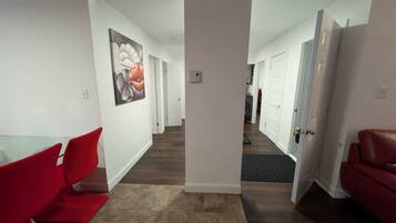 A modern hallway with a dining area on the left, a red couch on the right, and a door leading to another room.