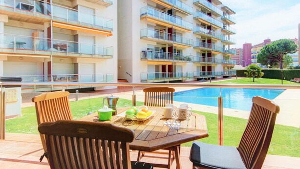 Ein Poolbereich im Freien mit einem Holztisch und Stühlen, umgeben von einem modernen Apartmenthaus mit Balkonen.