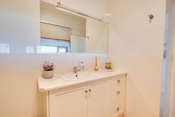 A bathroom with a white sink, mirror, and cabinets.