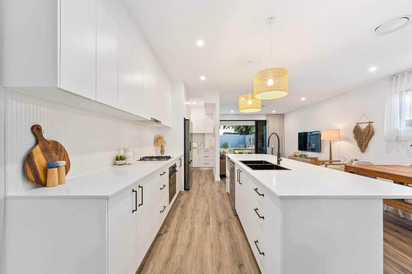A modern kitchen with white cabinetry, a central island, and a dining area with a wooden table.