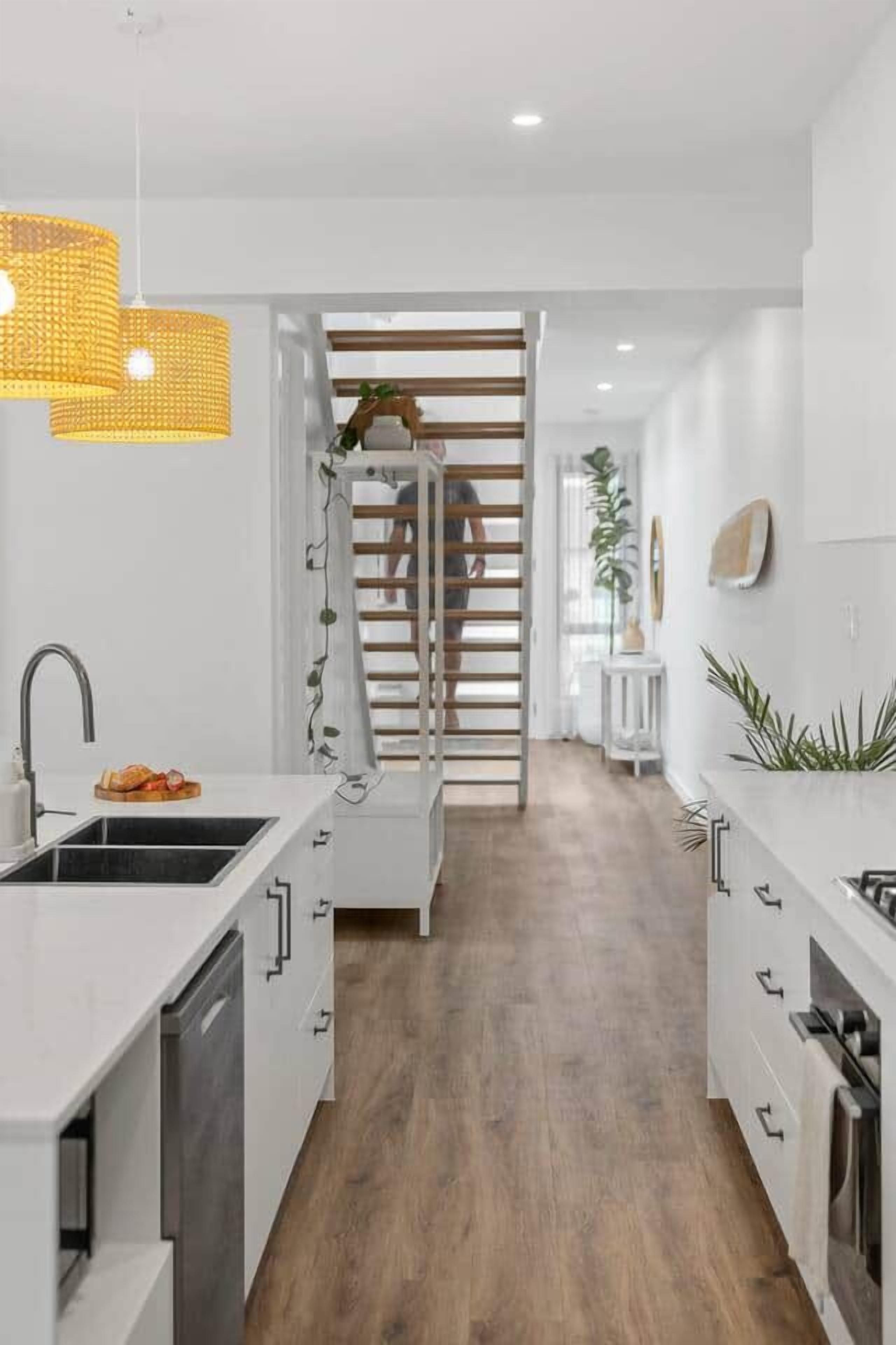 Una cocina moderna con armarios blancos, horno empotrado y escalera de madera que sube a otro nivel.