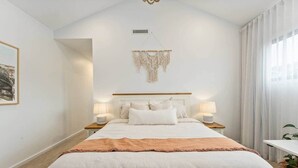 Una camera da letto con un letto grande, due comodini con lampade, un arazzo macramè e un quadro appeso al muro.