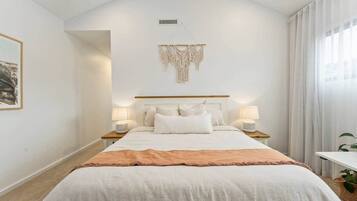 A bedroom with a large bed, two bedside tables with lamps, a macrame wall hanging, and a framed picture on the wall.