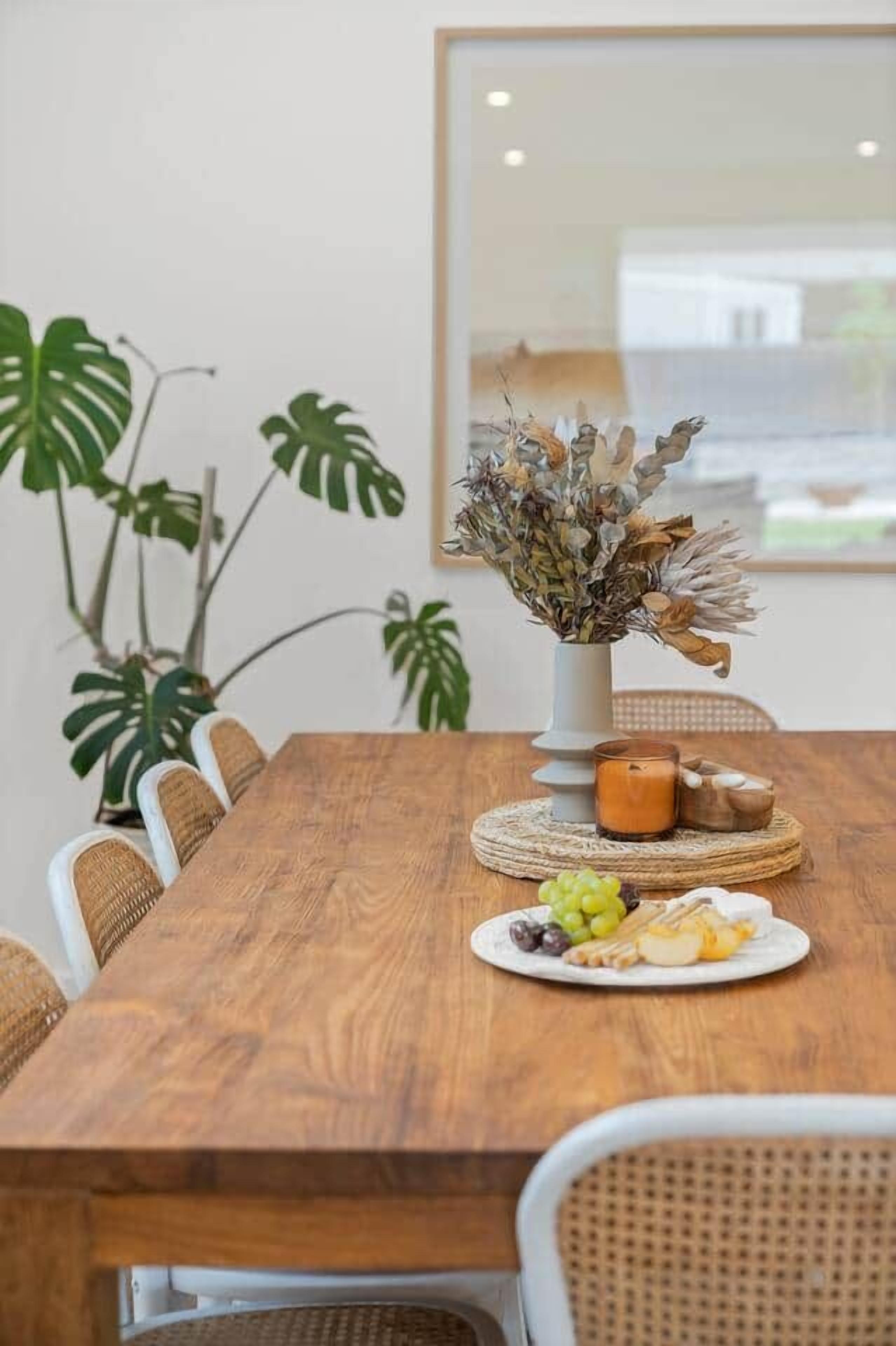 Una mesa de madera con un jarrón blanco, una vela y un plato de comida.
